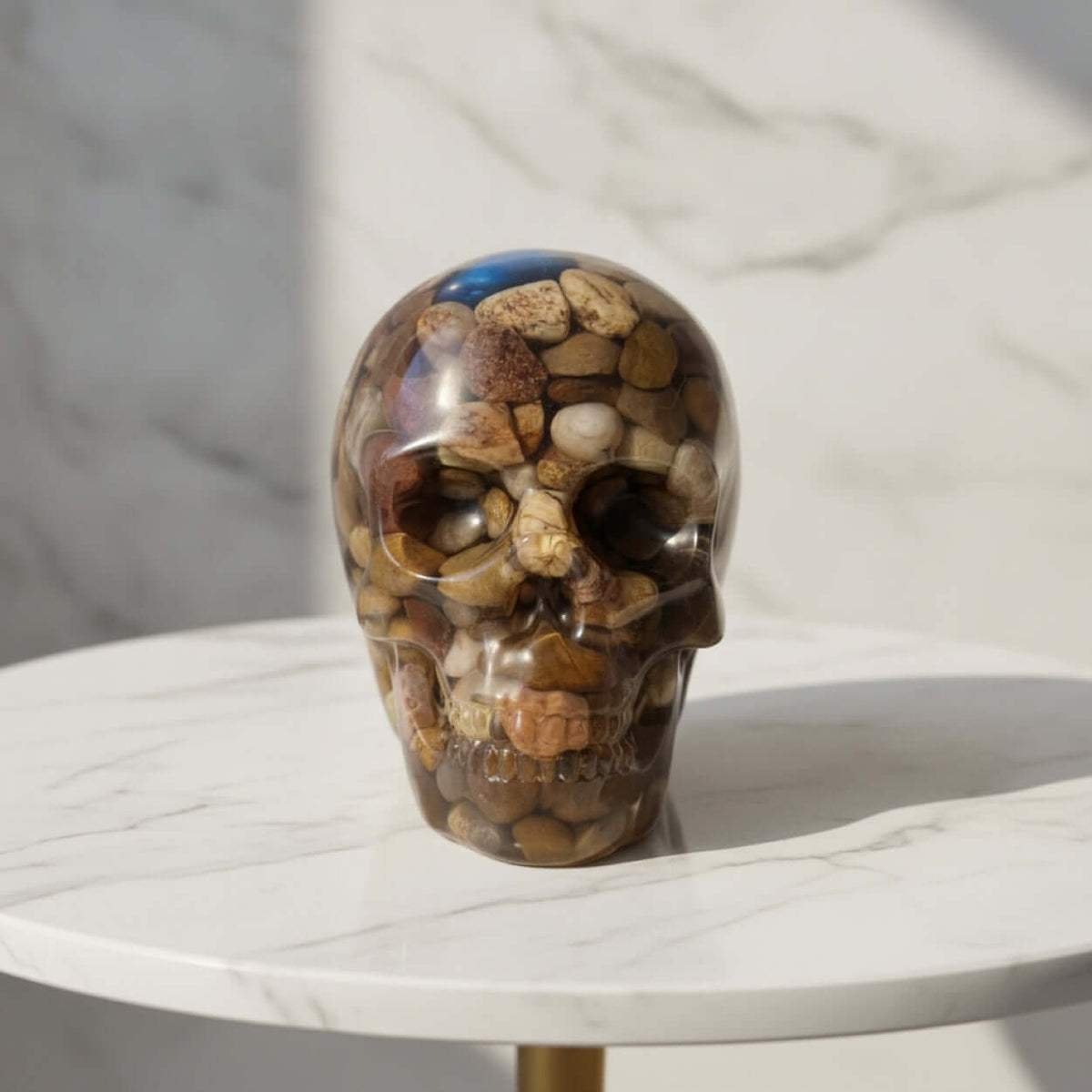 A Cosy Halloween - Skull-shaped clear resin ornament filled with natural-toned stones, displayed on a white round table.