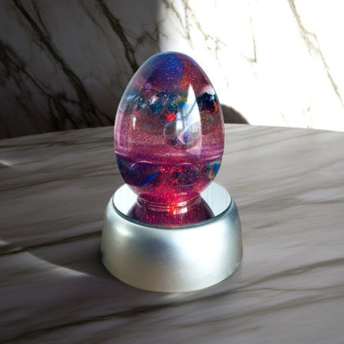 Colour changing egg filled with marbles on a reflective surface with light reflections