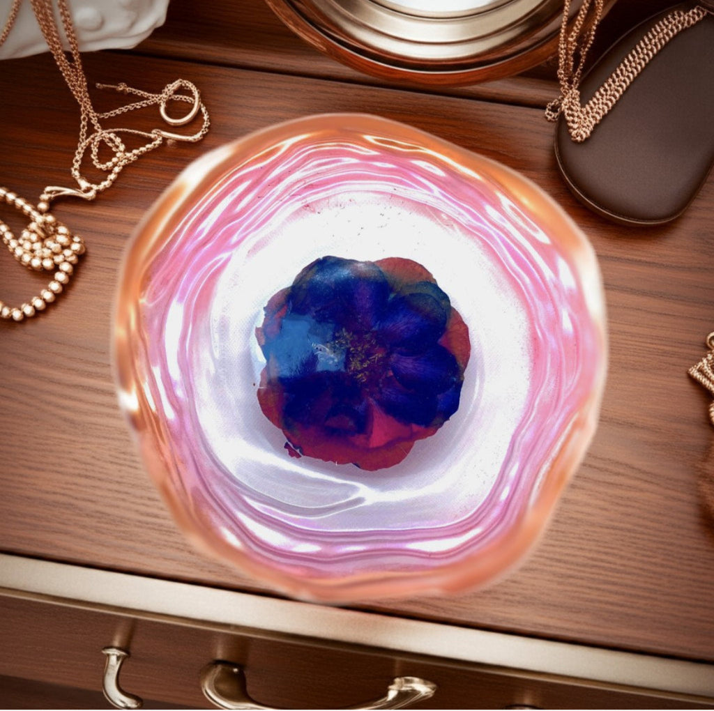 Decorative Trays - A round resin decorative tray with a swirling pink, white, and orange marbled pattern, containing a dark blue and red flower, displayed on a wooden surface with gold jewellery props.