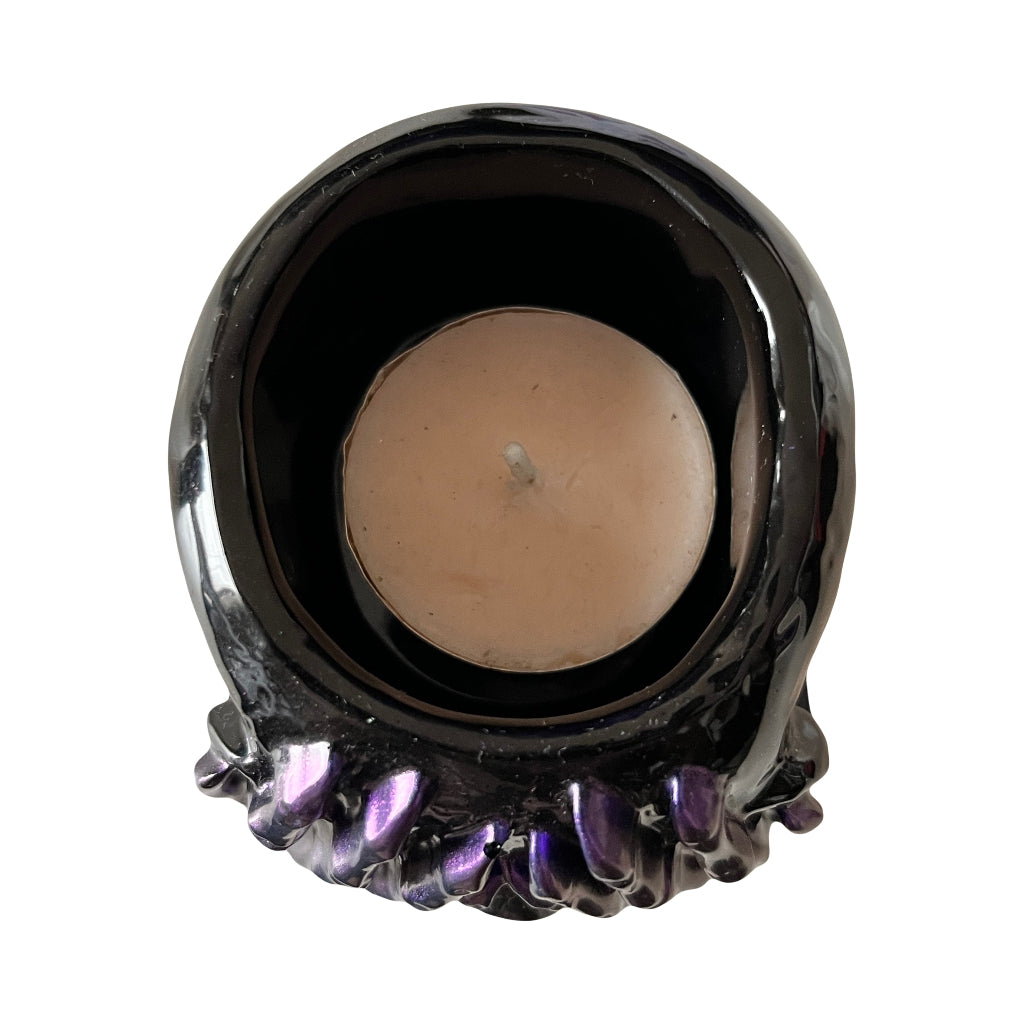 Resin Skull Pots - Top view of a black resin candle holder with a glossy finish and a textured, flower-like base with iridescent purple details, holding a lit tealight candle, shown against a plain white background.