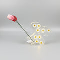 Bunny Bud Vase - A clear resin bunny figurine filled with small white daisy flowers and LED lights, with yellow centres, holding a pink tulip stem, photographed on a smooth light grey studio background.