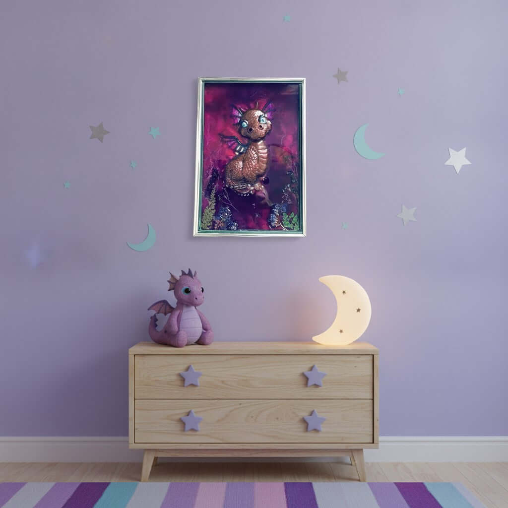 Framed artwork of a dragon with a colorful purple background on a lilac wall with stars and moons, above drawers with dragon and moon lamp. 