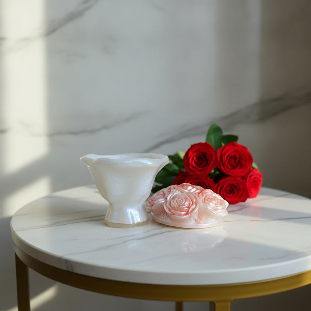 A white resin container and a pale pink rose-shaped lid, set on a round white marble table with gold legs, styled with red roses against a marble wall.