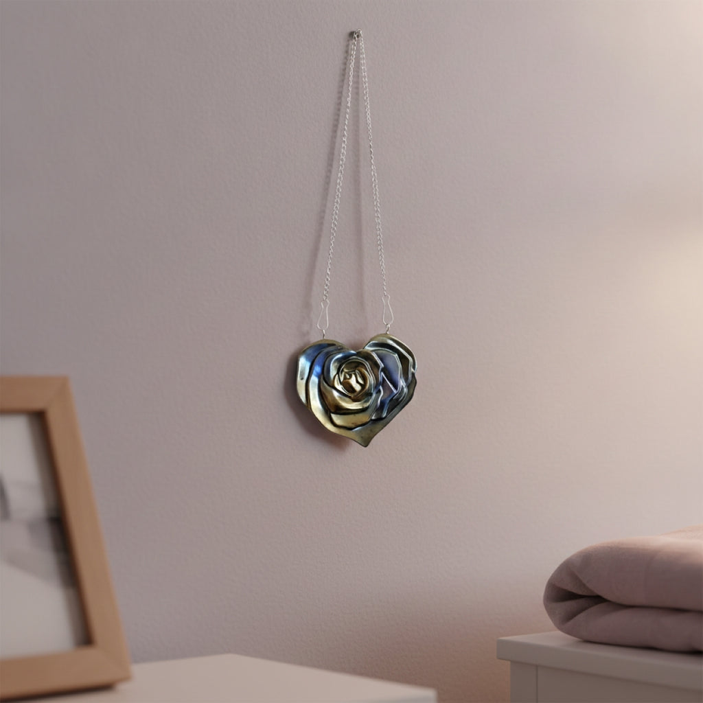 A metallic Heart Wall Decal hanging suspended from a hook on a light pink wall, with a small white table, framed art, and a pink blanket.