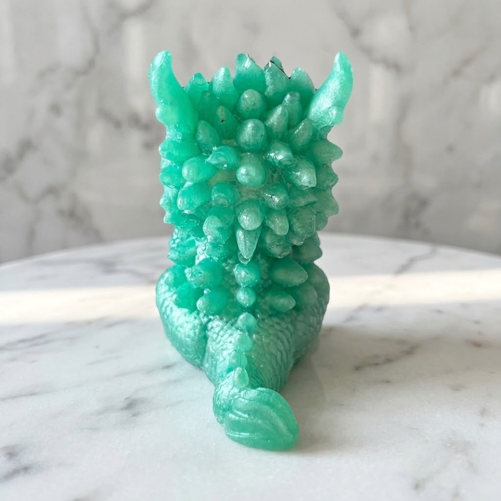 Baby Dragon Figurines - Back view of a small translucent mint green dragon figurine with textured scales and spiky back details, photographed on a white marble surface with a matching marble background.