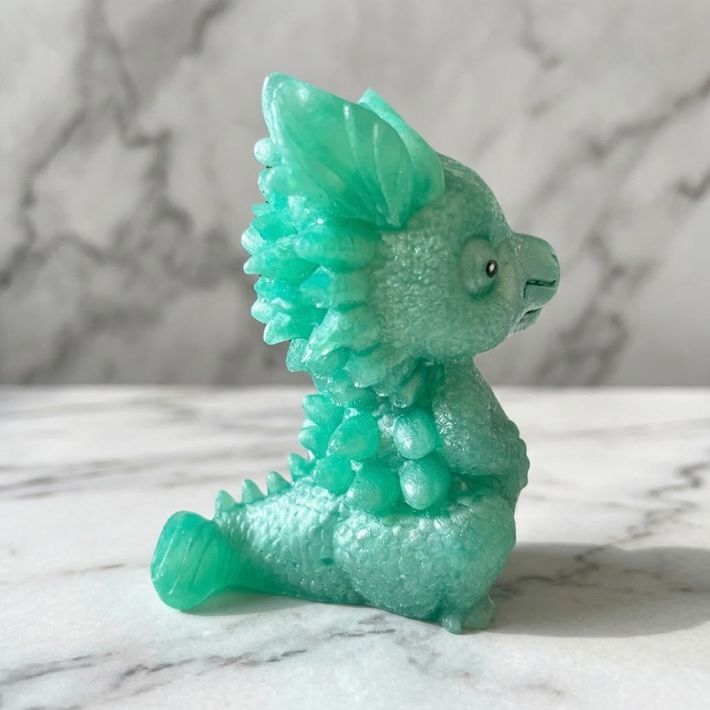Baby Dragon Figurines - Side view of a  small translucent mint-green dragon figurine sitting on a white marble surface with a grey marble background.