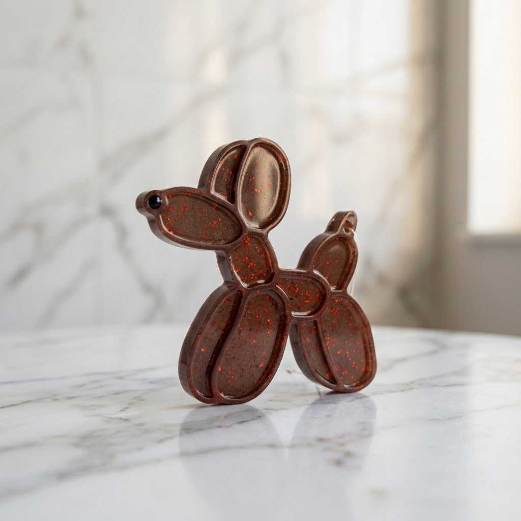 Balloon Dog Figurine - A small dog-shaped decorative object with a glossy dark brown finish and scattered red speckles, standing on a white marble surface against a softly blurred marble background.