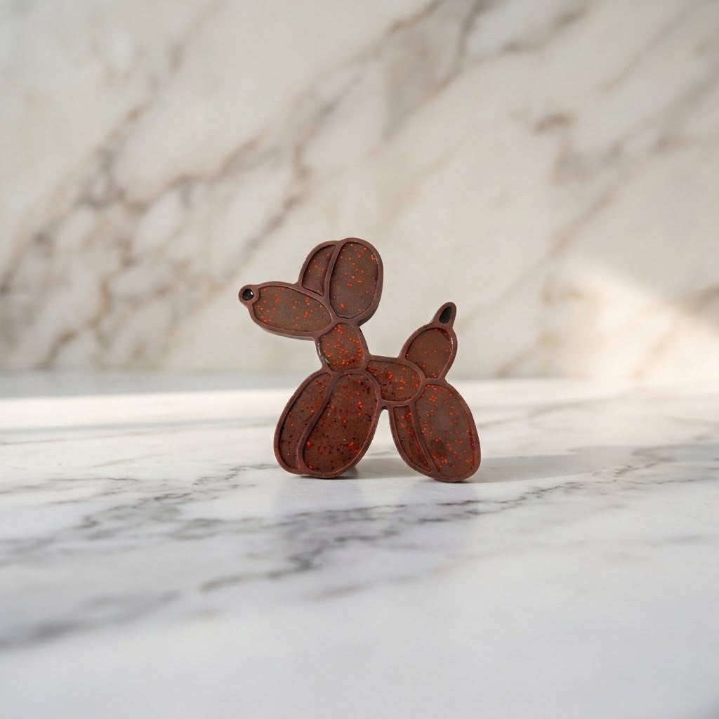 Balloon Dog Figurine - A small dog-shaped decorative object with a distressed rusted brown finish and red glitter, standing on a white marble surface with a matching marble background.