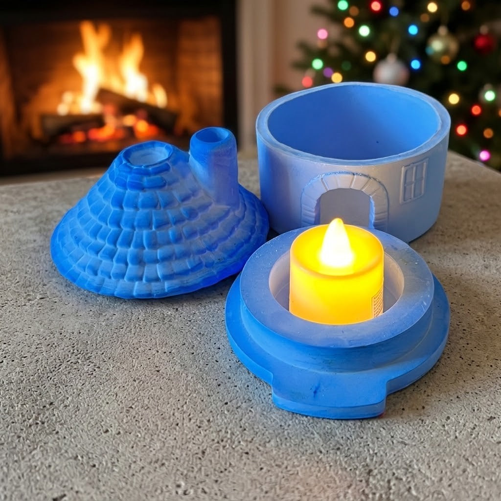 Candle Holder Houses - A small blue house roof with chimney, blue base with lit candle and middle of circular house with archway door.  Placed on a round stone table in front of a cosy fireplace and a blurred Christmas tree.