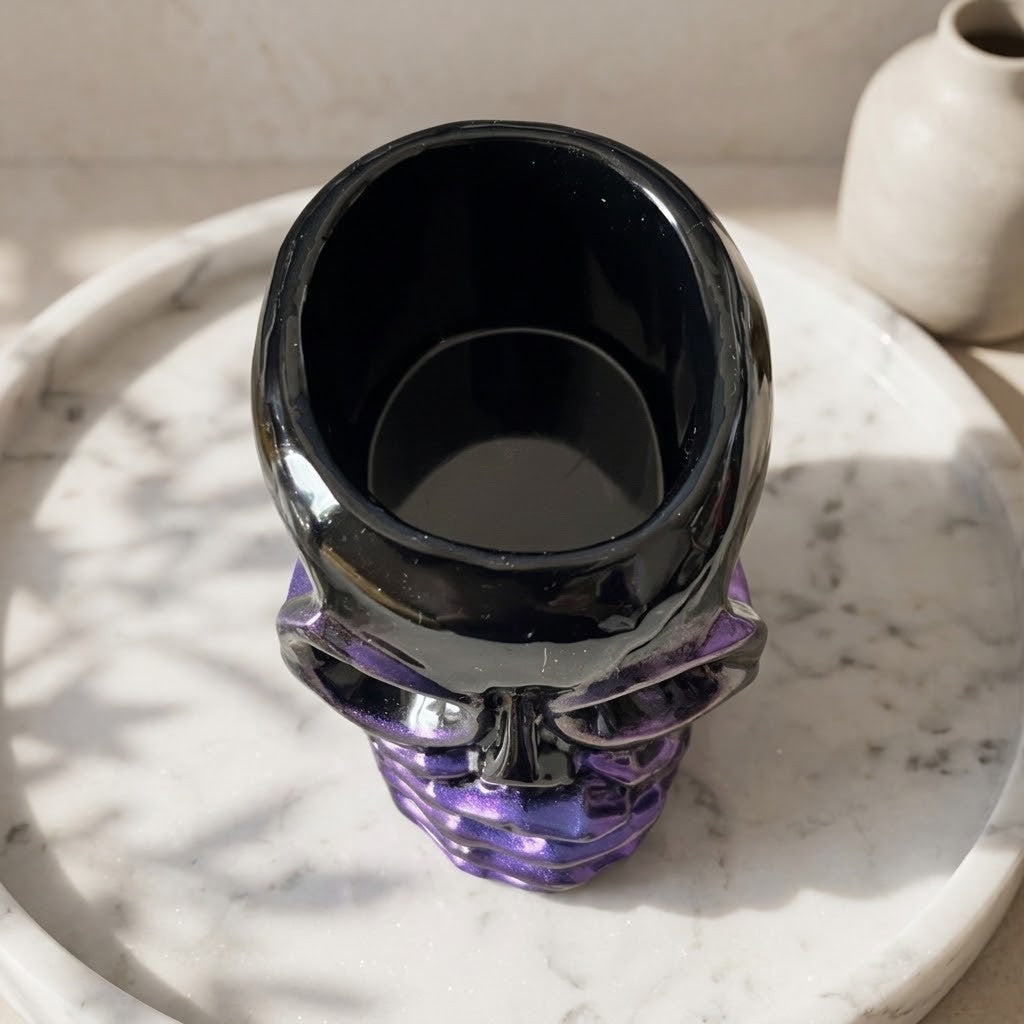 Resin Skull Pots - A skull-shaped glass vase with a glossy black upper portion and a translucent purple lower portion, displayed on a white marble tray.