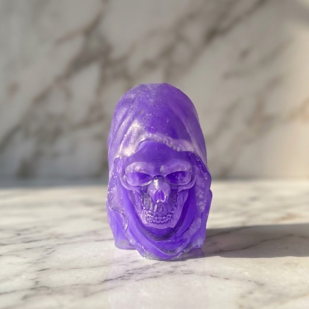 Hooded Skull Figurines - A small carved purple resin skull figurine with a hood, standing on a white marble surface with a blurred marble background.
