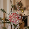 Novelty Christmas Tree Decorations - A clear resin snowflake Christmas ornament with red glitter lettering that reads f*** hanging from a pine tree branch in a decorated indoor setting.