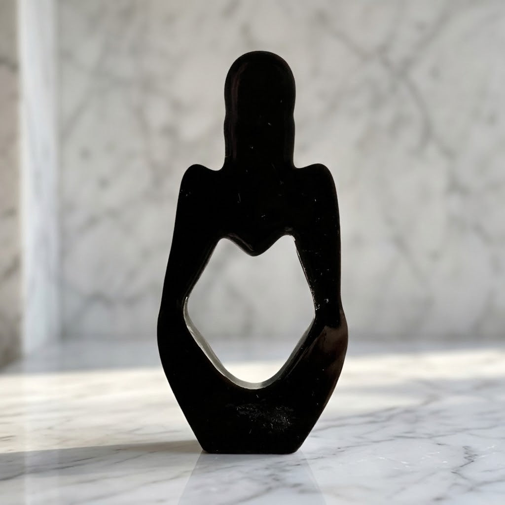 Nordic Resin Thinker - Back view of a black resin figurine of a seated figure with a heart-shaped cut-out in the centre, displayed on a white marble surface against a marble background.