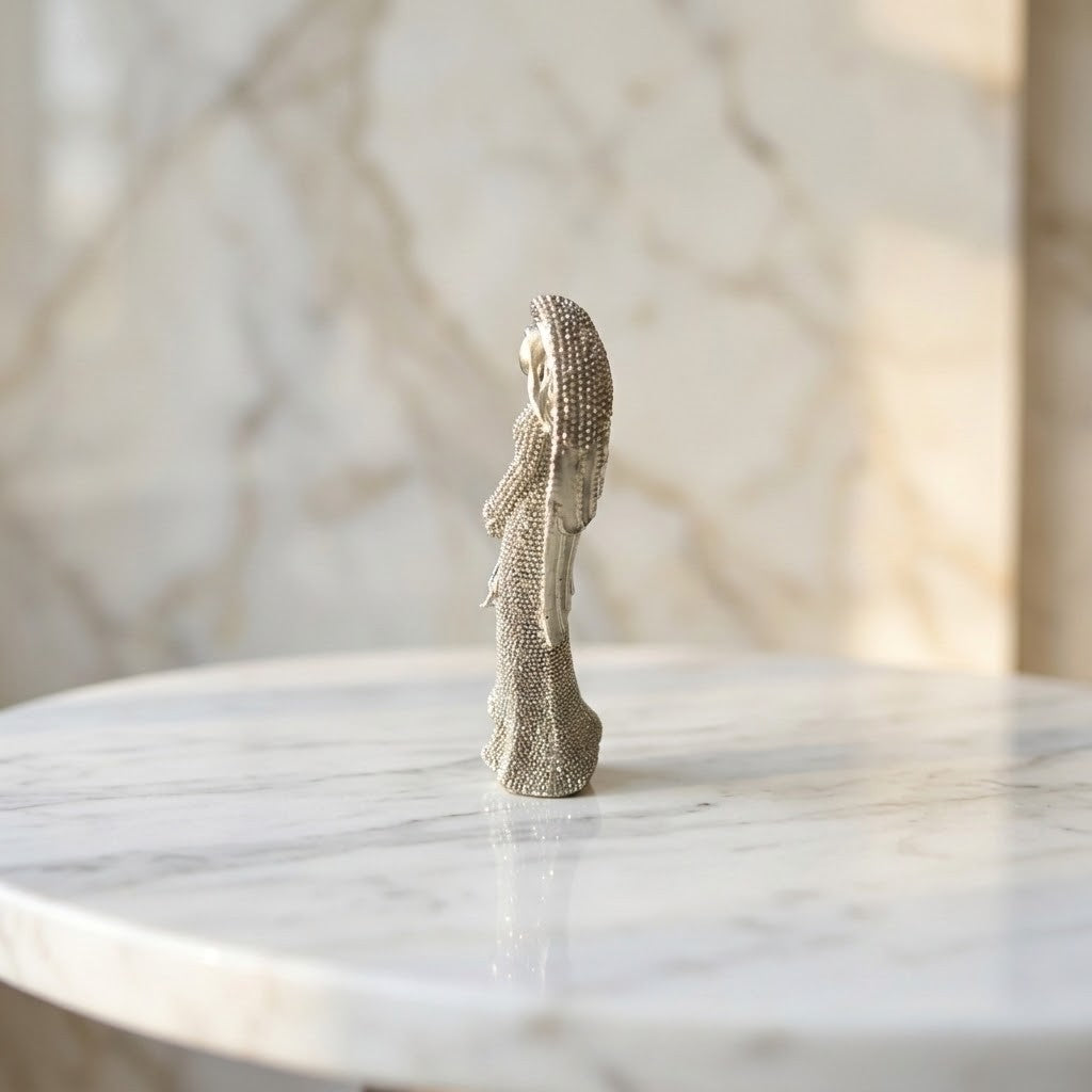 Christmas Angel Figurine - Side view of a small metallic angel figurine with a textured, glittering finish, standing on a white marble table against a matching marble background.