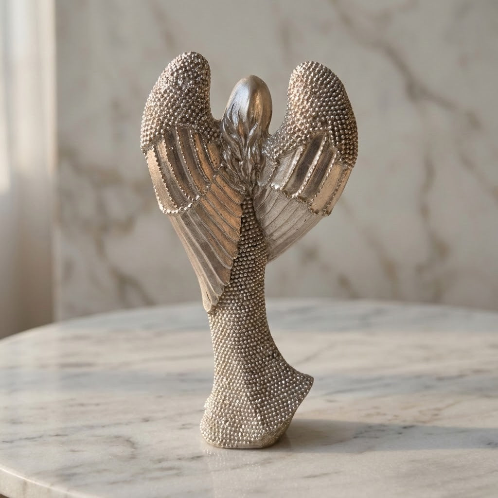 Christmas Angel Figurine - Back of a metallic silver angel figurine with textured wings and a beaded body, displayed on a round marble table against a marble wall background.