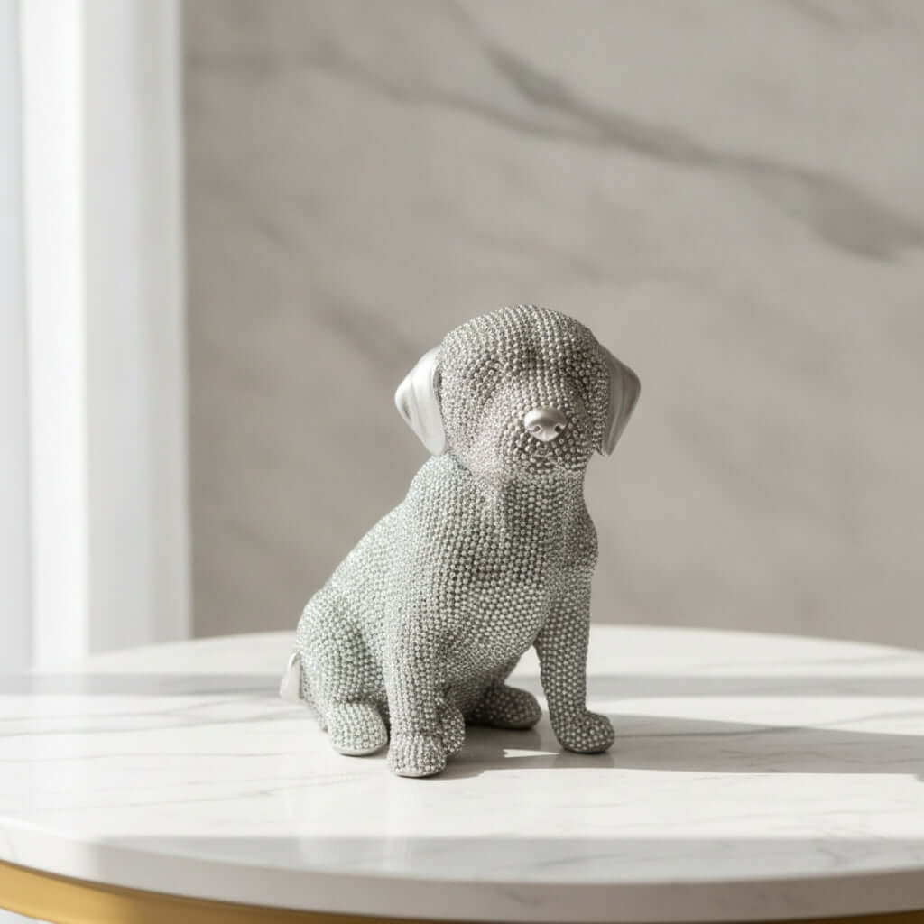 A textured silver dog figurine in a light gray tone, sitting on a white marble table against a marble wall background.