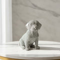 A textured silver dog figurine in a light gray tone, sitting on a white marble table against a marble wall background.