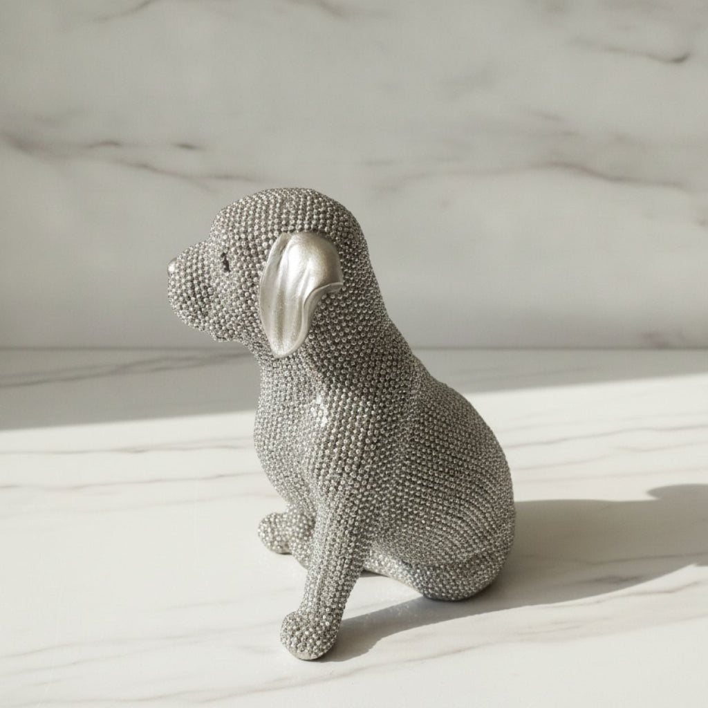 A silver dog figurine covered in small rhinestones, sitting on a white marble surface with a matching marble background.