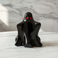 Ghost Figurine Ornaments - A glossy black ghost figurine with glowing red eyes, standing on a white marble surface against a matching marble background.