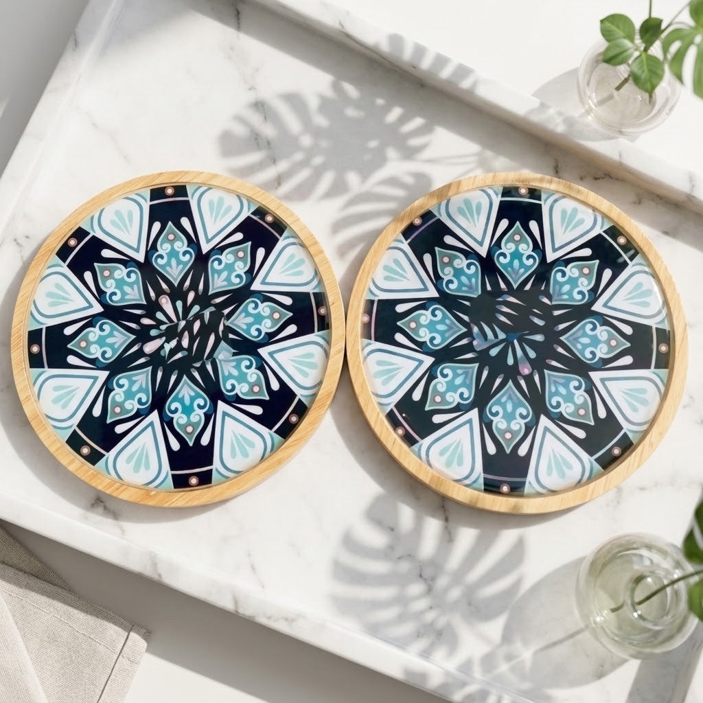 Mandala Bamboo Coasters - Two round coasters with a light wood base and a colourful geometric mandala pattern in navy, teal, and white, displayed on a white marble tray.