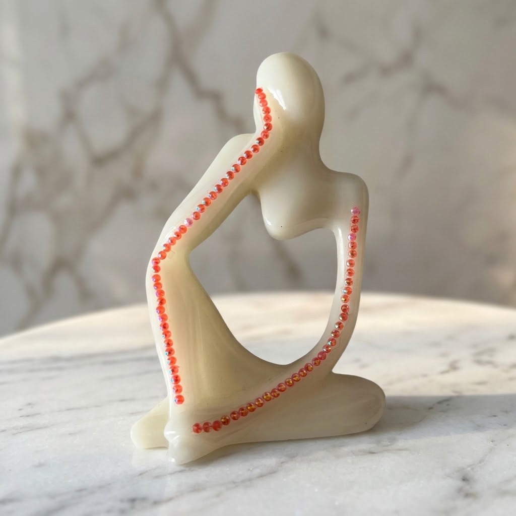 Nordic Resin Thinker Figurine - A minimalist cream-colored resin figurine of a seated woman, decorated with small pink bead accents along the outline, displayed on a white marble surface with a marble-patterned background.