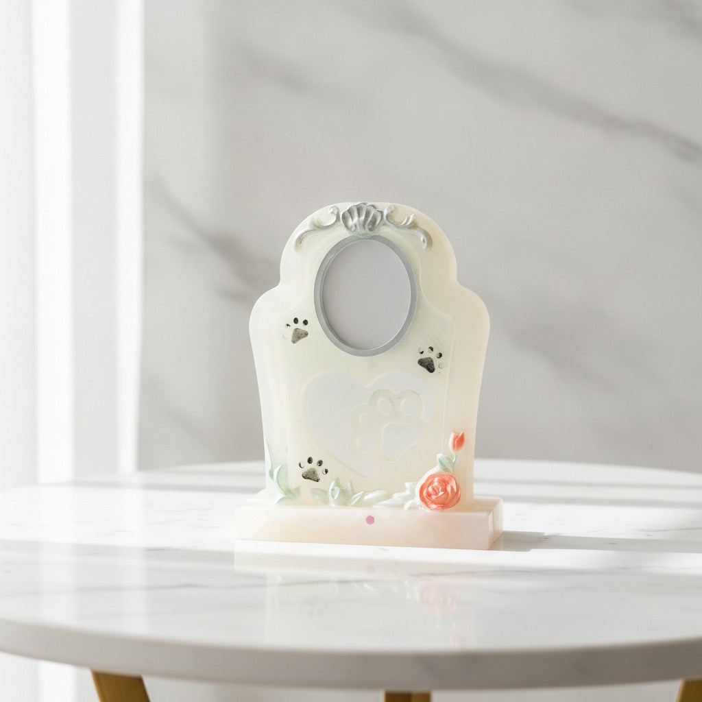 Pet Memorial - A small decorative tabletop photo frame with a cream-colored arched body, paw-print motifs, a floral accent, and a rectangular base, displayed on a white marble table against a light marble wall.