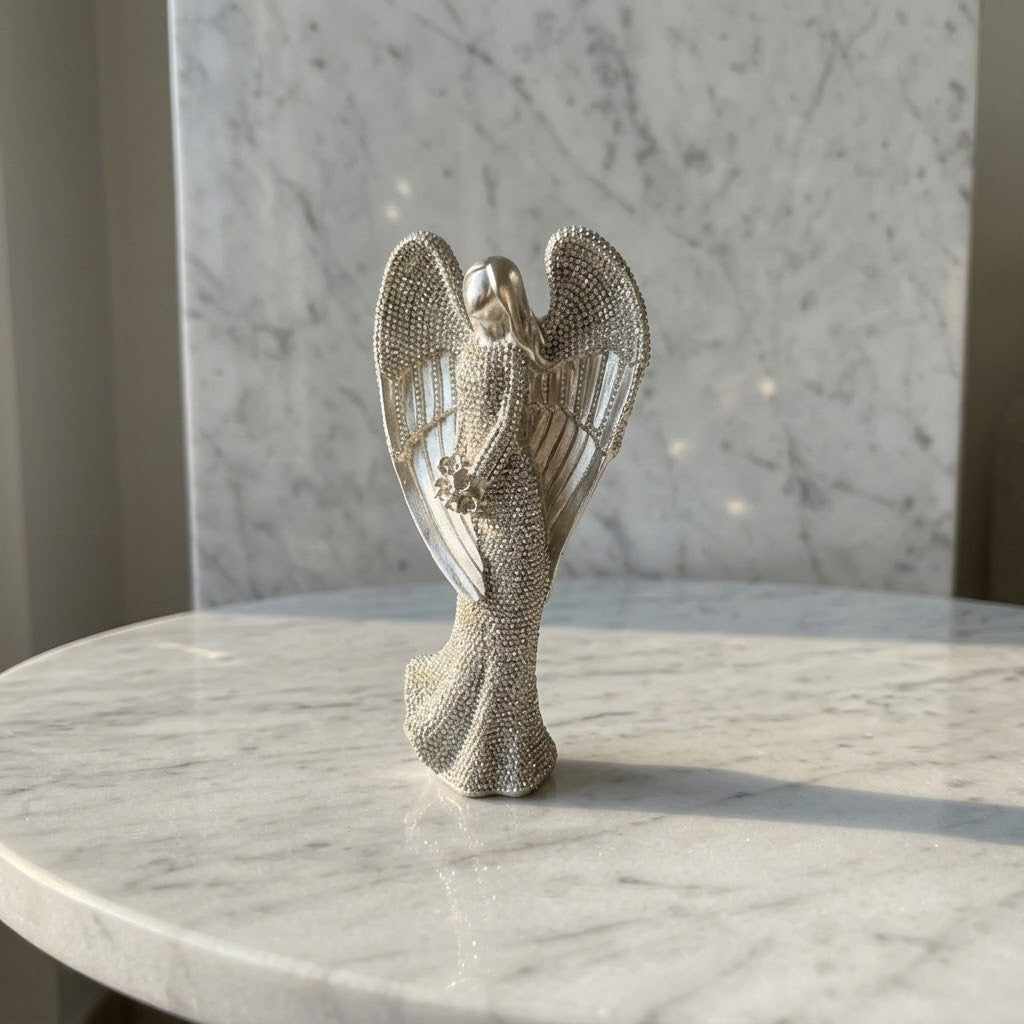 Christmas Angel Figurine - A silver-toned angel figurine with detailed textured wings and a flowing gown, displayed on a white marble table against a marble wall.