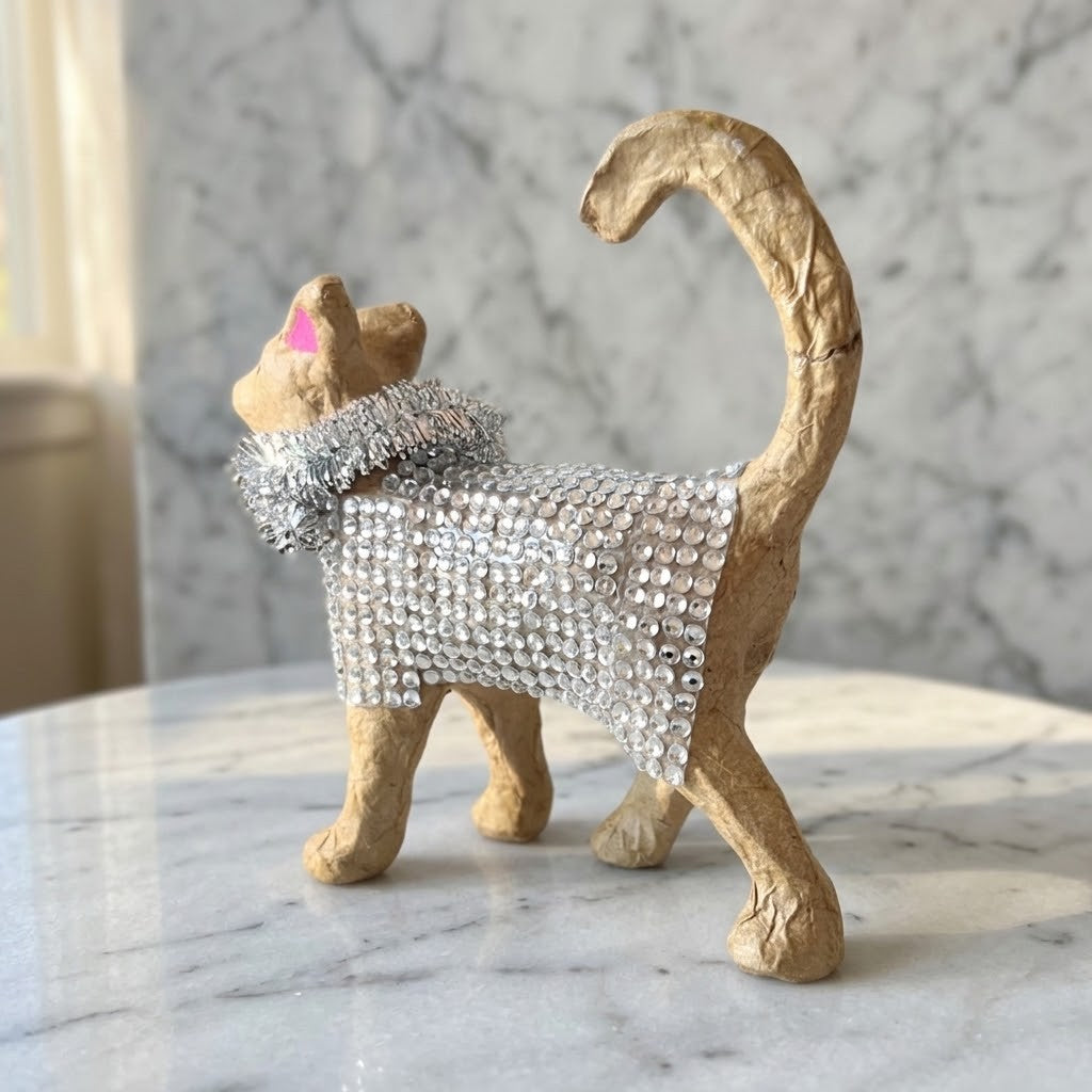 Diamante Cat Figurine - A small tan cat figurine wearing a sparkling silver rhinestone collar and a matching silver rhinestone body wrap, standing on a white marble surface against a grey marble wall.