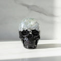 A glossy black Skull figurine decorative object with a translucent blue flower embedded inside, displayed on a marble surface.
