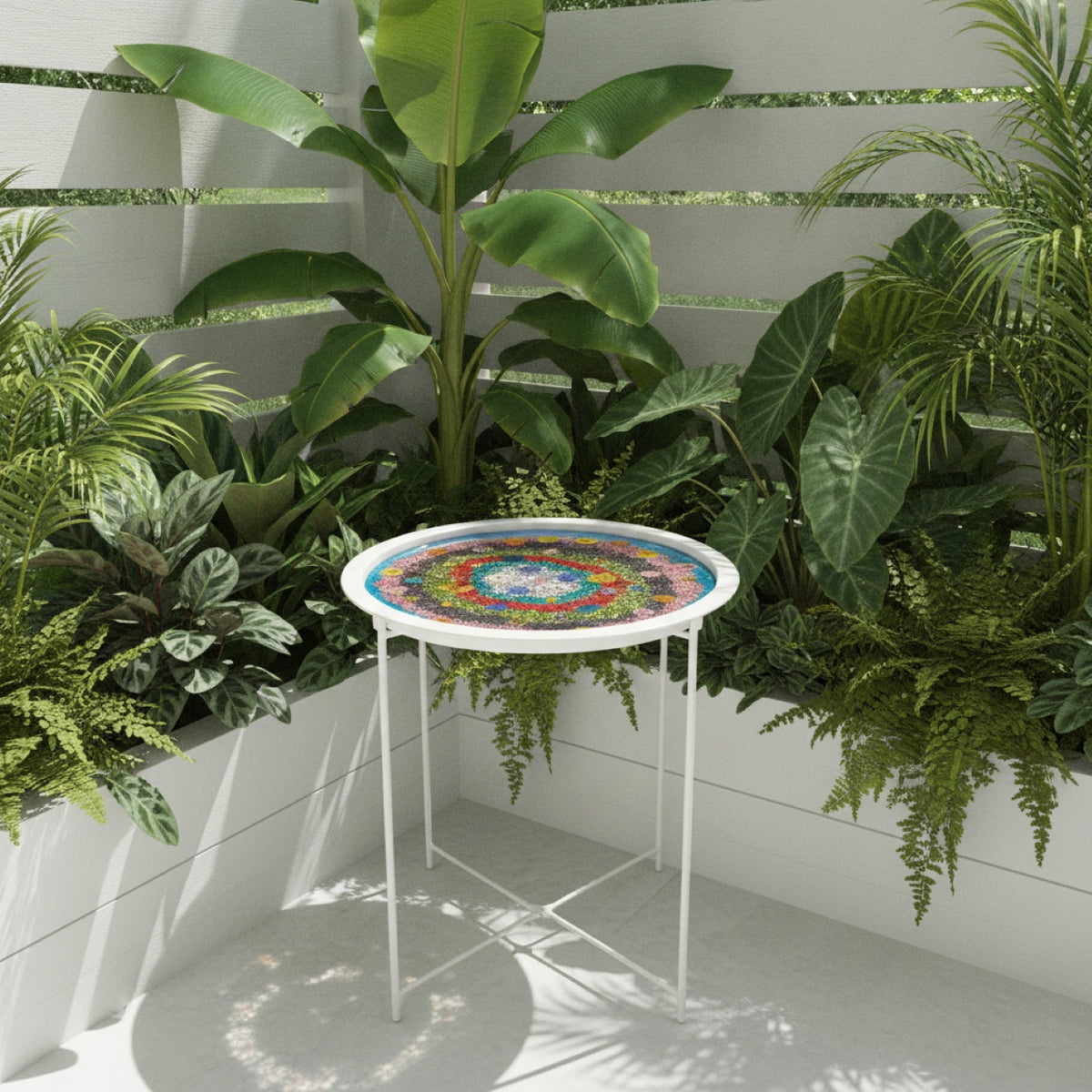 A small round white metal side table with a colorful glitter and flowers top, styled in a lush green outdoor garden corner.