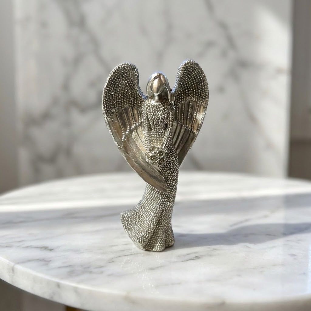 Christmas Angel Figurine - A textured silver angel figurine with outstretched wings, standing on a white marble surface with a blurred marble background.