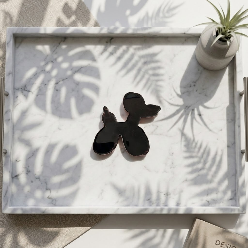Balloon Dog Figurine - Back view of a glossy black balloon dog-shaped tray insert resting on a white marble serving tray with silver handles, styled with a small potted plant and leaf shadows.