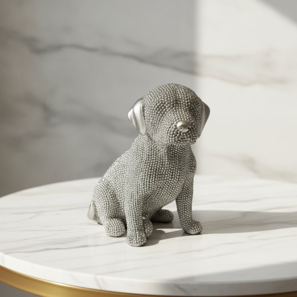 A silver dog figurine with a textured, beaded surface, sitting on a white marble-topped table against a matching marble background.