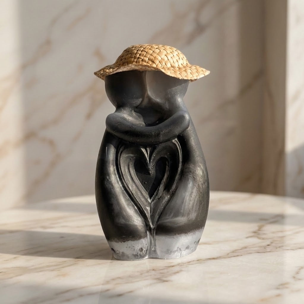 Hugging Couple Figurine - A sculptural decorative figurine of two embracing figures with a woven straw hat, shown on a light marble surface against a marble wall.