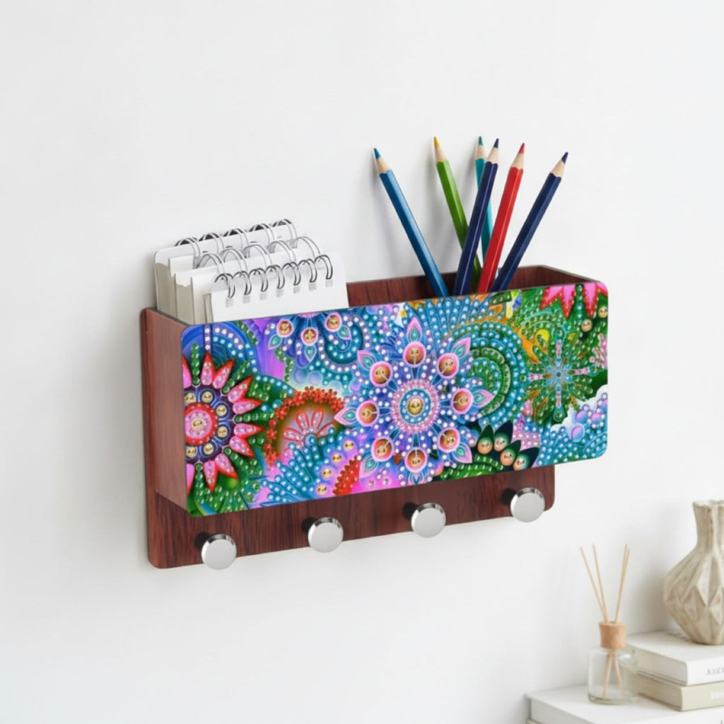 A wall-mounted wooden Storage Rack Box with a colorful mandala-patterned front panel, holding spiral notebooks and colored pencils, with four silver hooks below, shown against a white wall.