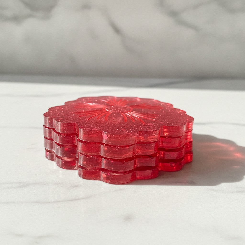 Flower shaped coasters - A stack of four translucent red resin coasters with a scalloped edge and a sunburst pattern in the centre, resting on a white marble surface.