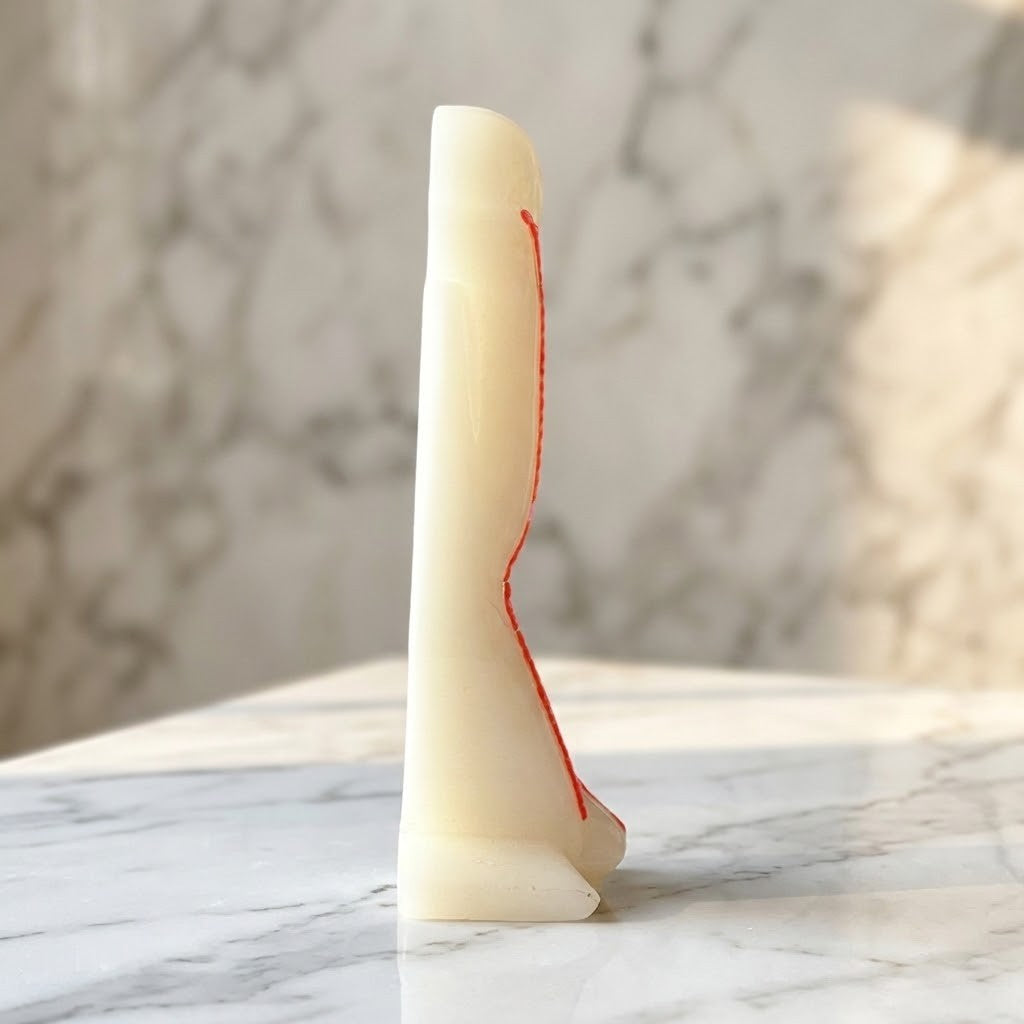 Nordic Resin Thinker  Figurine - A side view of a cream-colored resin decorative object with a curved shape and a thin red line running vertically along the side, displayed on a white marble surface against a blurred marble background.