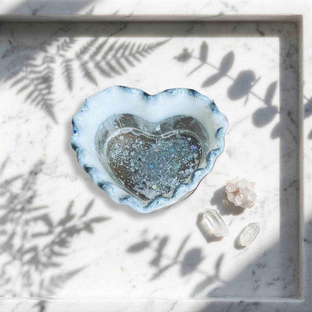 Heart Shaped Trinket Jar - A heart-shaped resin dish with a silver and white marbled rim, filled with glittery silver holographic resin, displayed on a white marble tray with leaf shadows. 