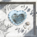 Heart Shaped Trinket Jar - A heart-shaped resin dish with a silver and white marbled rim, filled with glittery silver holographic resin, displayed on a white marble tray with leaf shadows. 