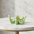 A light green novelty octopus figurine item with a yellow head and large cartoon eyes, with a middle finger pointing upwards a white marble table with a gold-toned rim against a soft marble wall background.