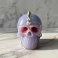 Studded Gothic Skull - A small glossy skull-shaped object in pale lavender with metallic silver spikes on top, photographed on a light marble surface against a marble background.